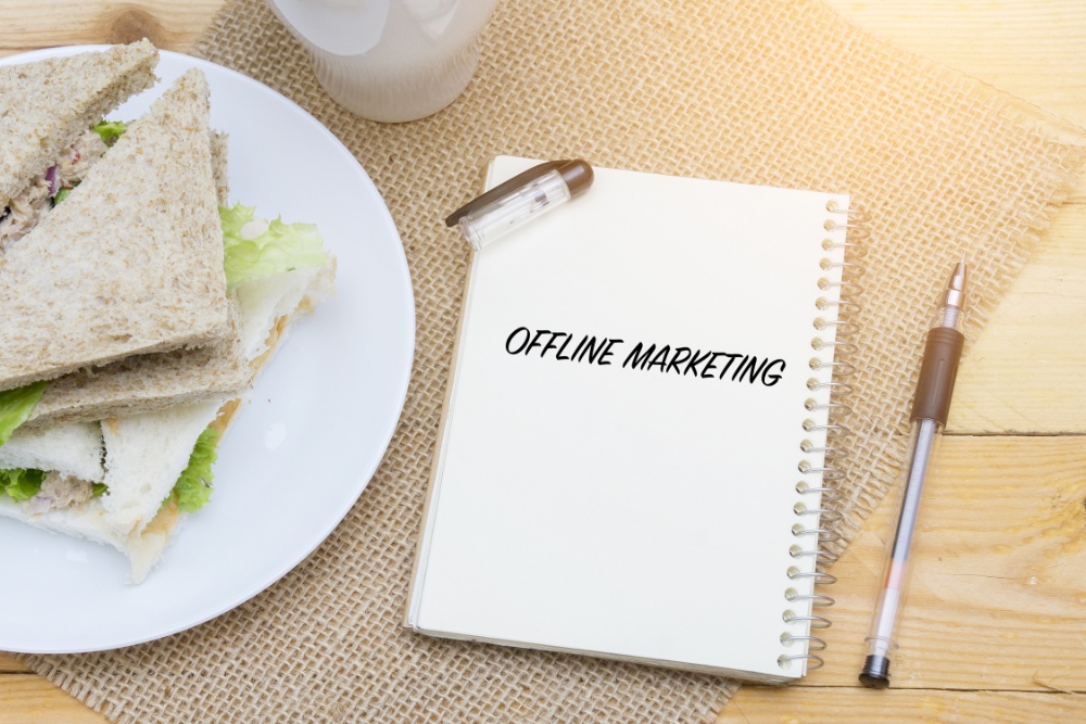 kanapka na stole a obok notes z napisem offline marketing